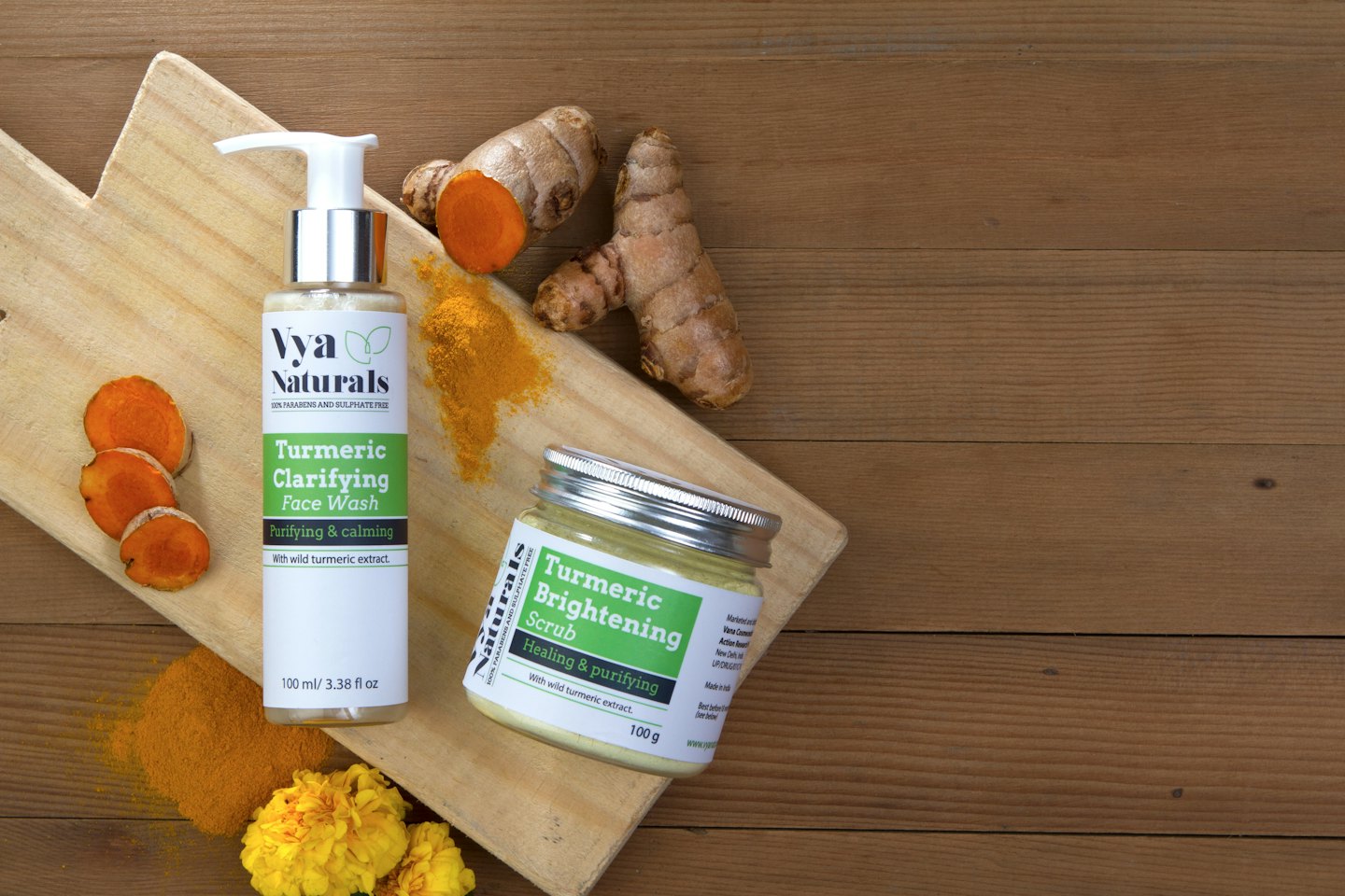Turmeric skincare products arranged with fresh turmeric and yellow flowers.